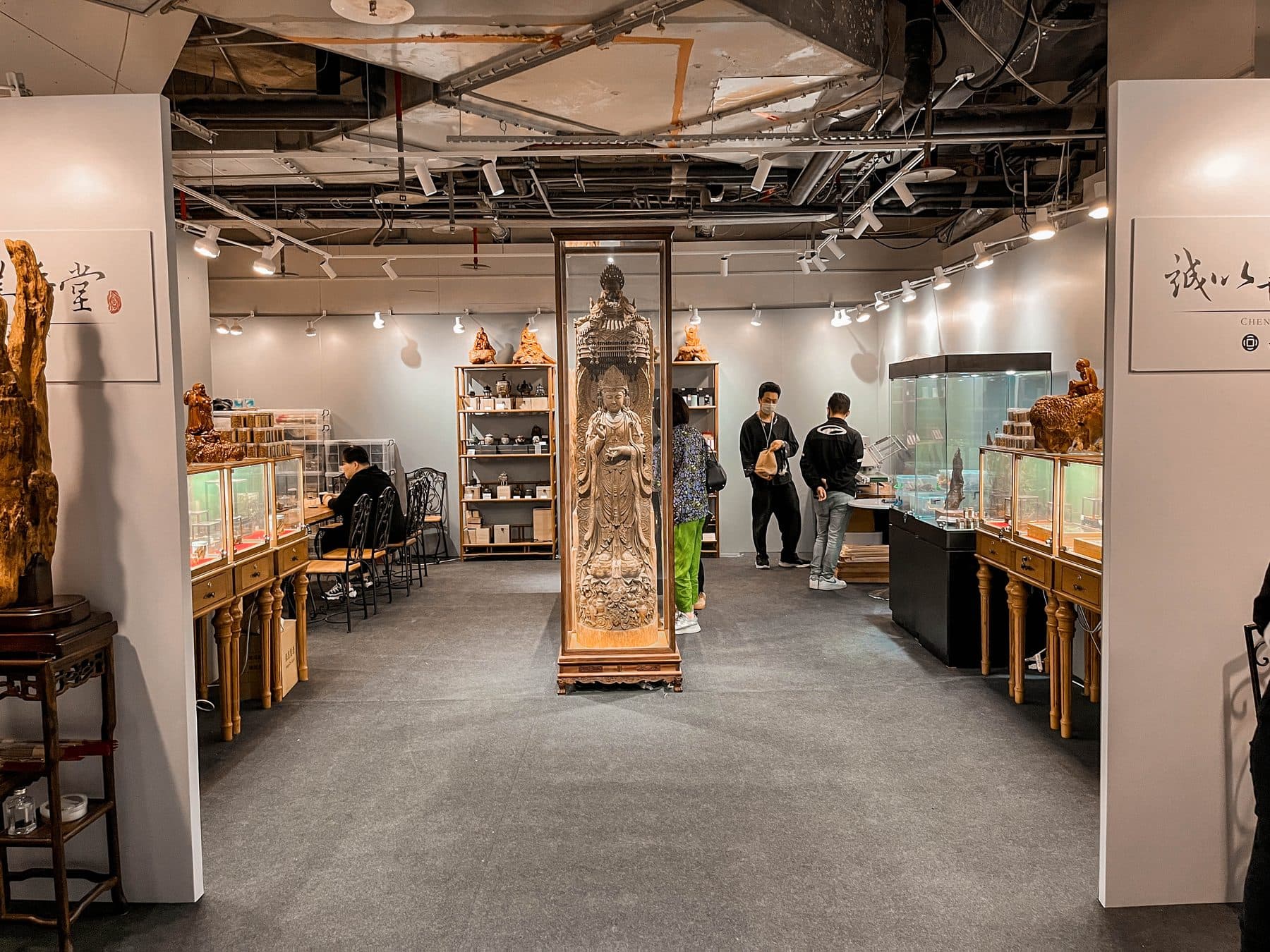 展場全景，一整排玻璃櫃擺滿沉香雕件，中間立著觀音像